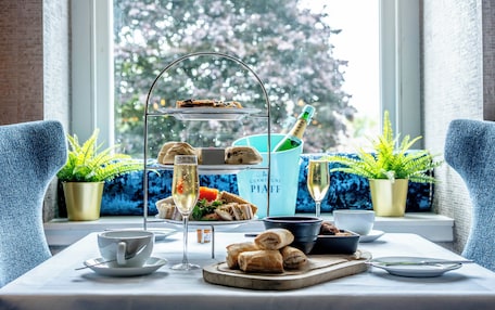 A table set for a tea service with sandwiches, pastries, and a bottle of champagne.