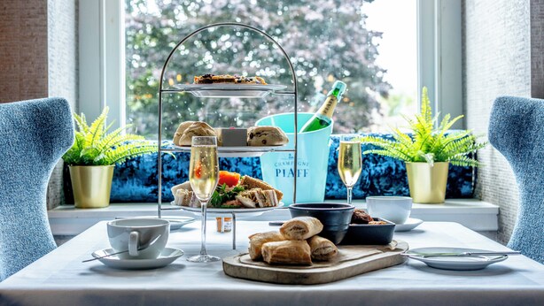 A table set for a tea service with sandwiches, pastries, and a bottle of champagne. - Colessio (Stirling)