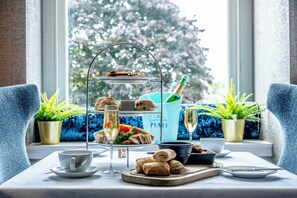 A table set for a tea service with sandwiches, pastries, and a bottle of champagne. - Colessio (Stirling)