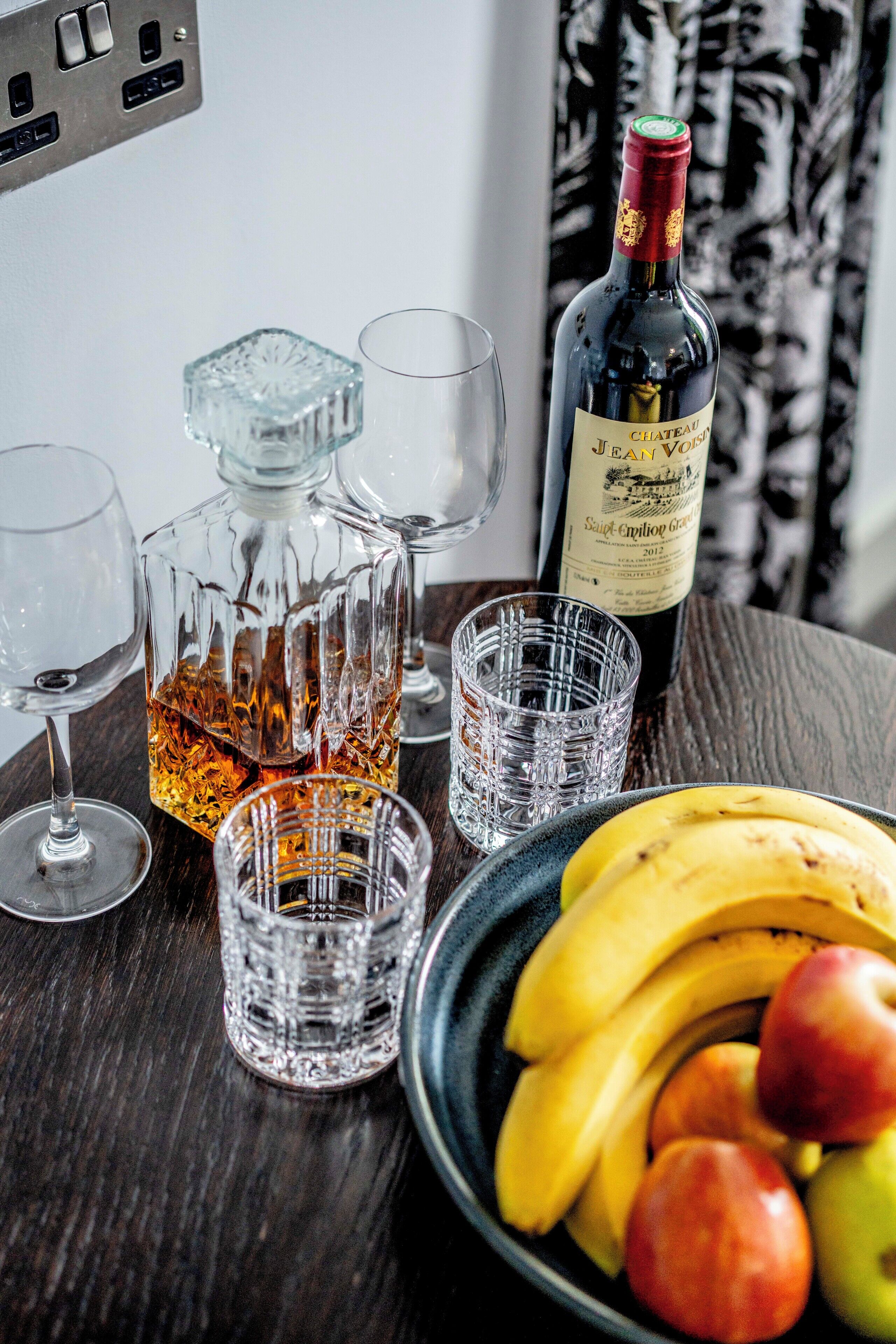 A bottle of Chateau Mouton Rothschild wine, a decanter, and glasses on a wooden table with a bowl of fruit.