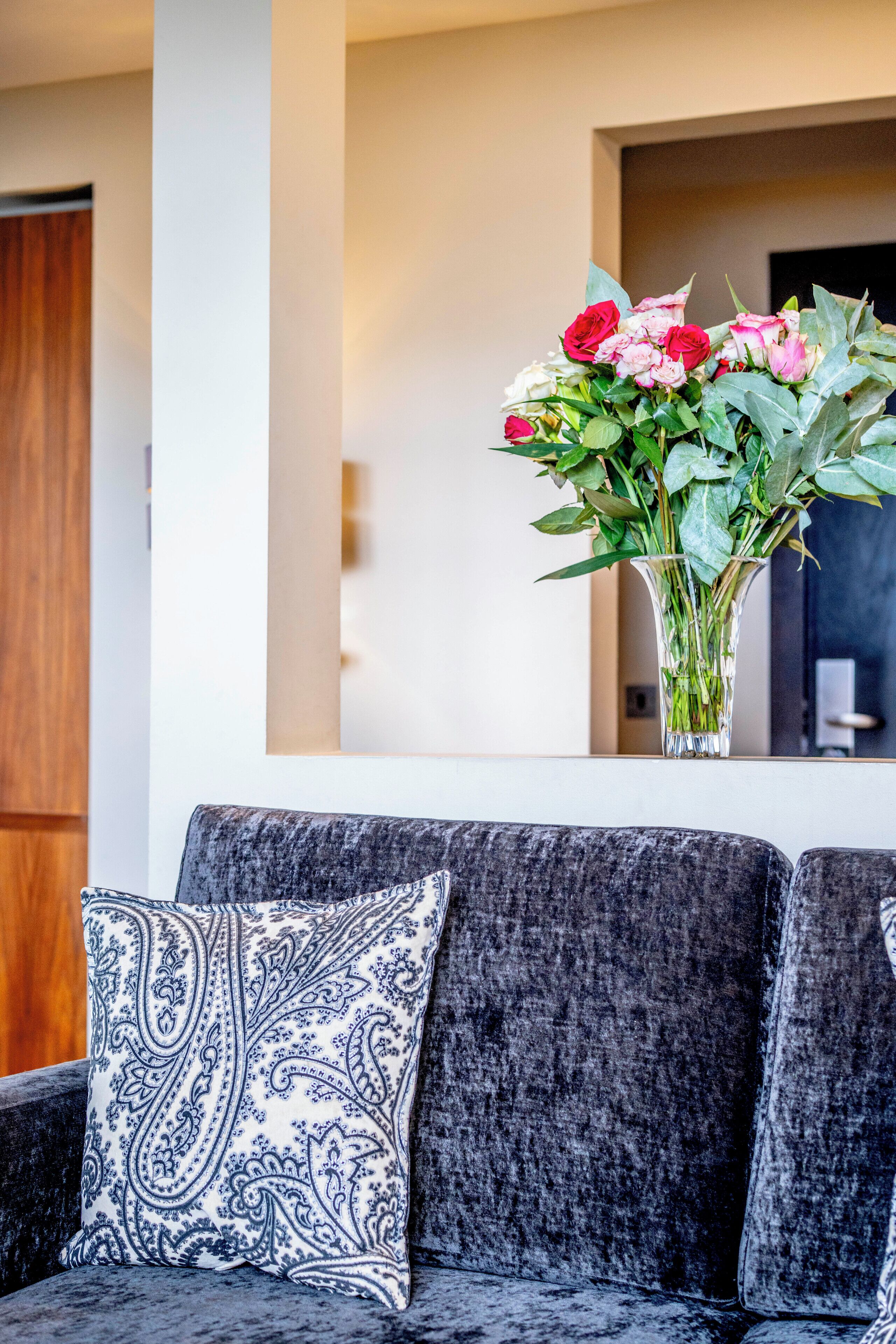 A modern living room with a grey sofa, a patterned throw pillow, and a vase of flowers on a white console table.