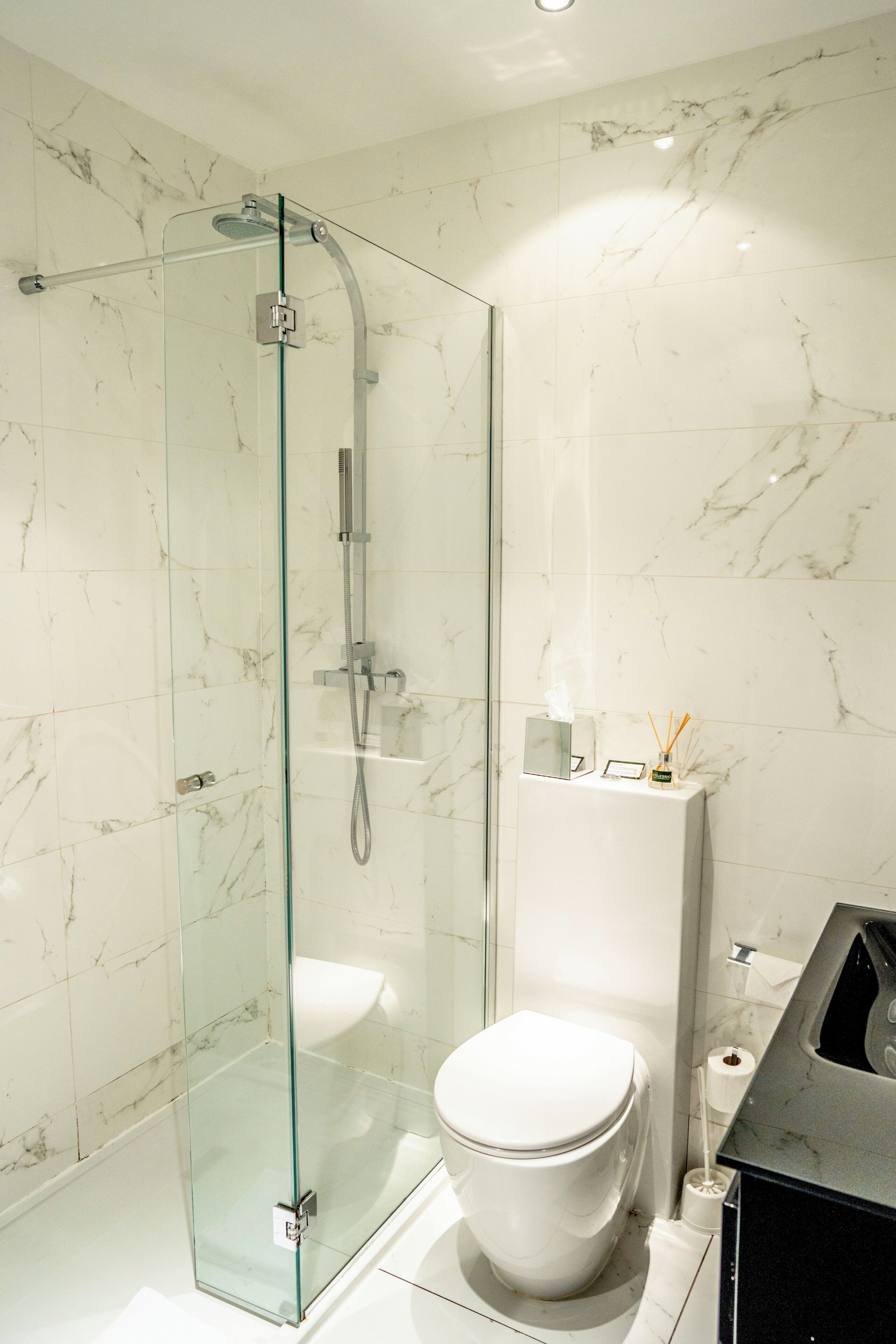 A modern bathroom with a glass-enclosed shower, a white toilet, and a marble-tiled wall.