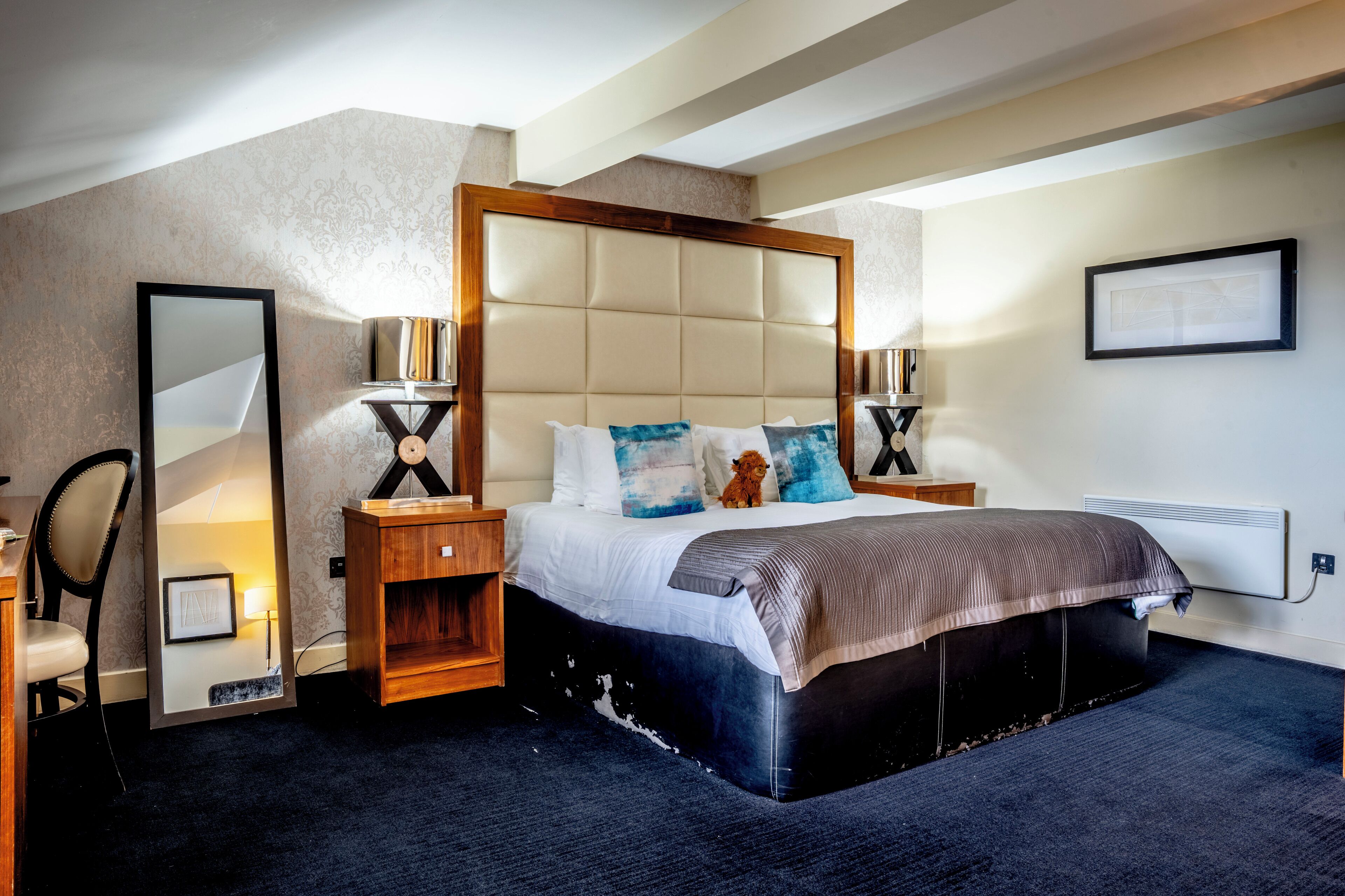 A modern bedroom with a large bed, wooden headboard, two bedside tables, a mirror, and a framed picture on the wall.