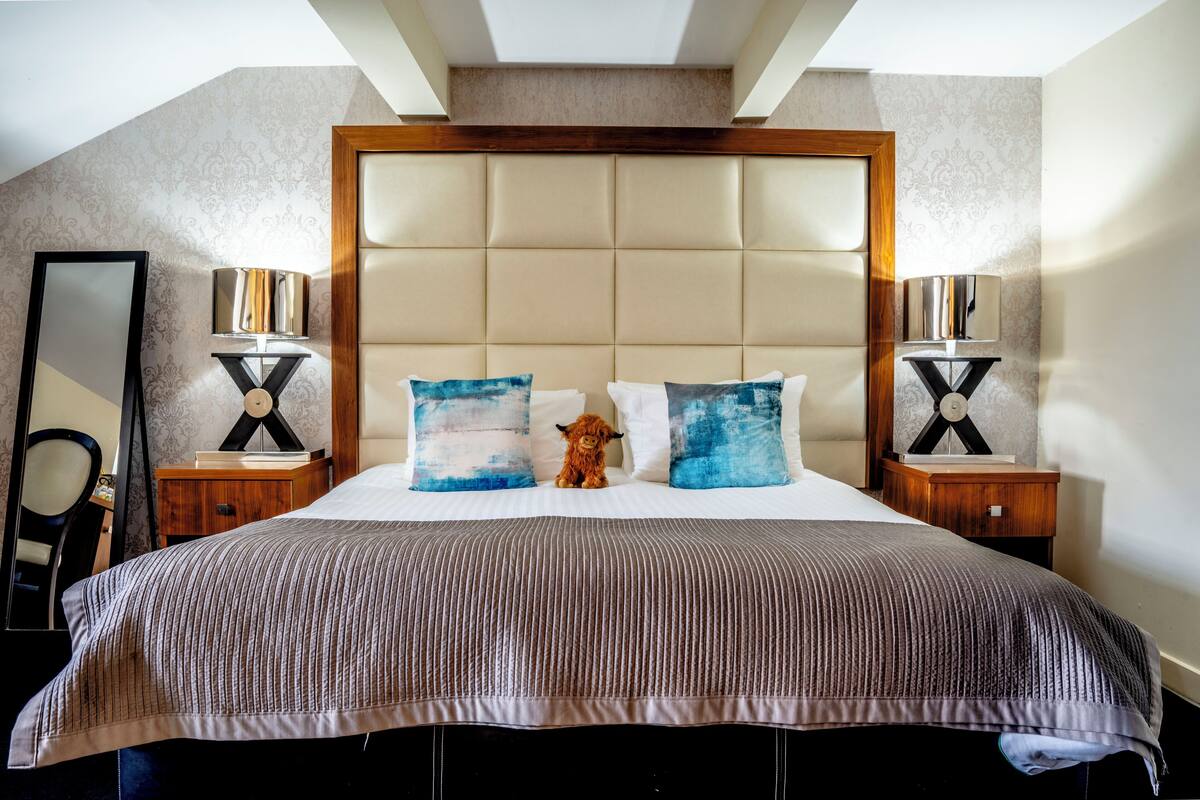 Une chambre d’hôtel avec un grand lit, deux tables de chevet, une petite table, un miroir et une petite figurine décorative représentant un animal.