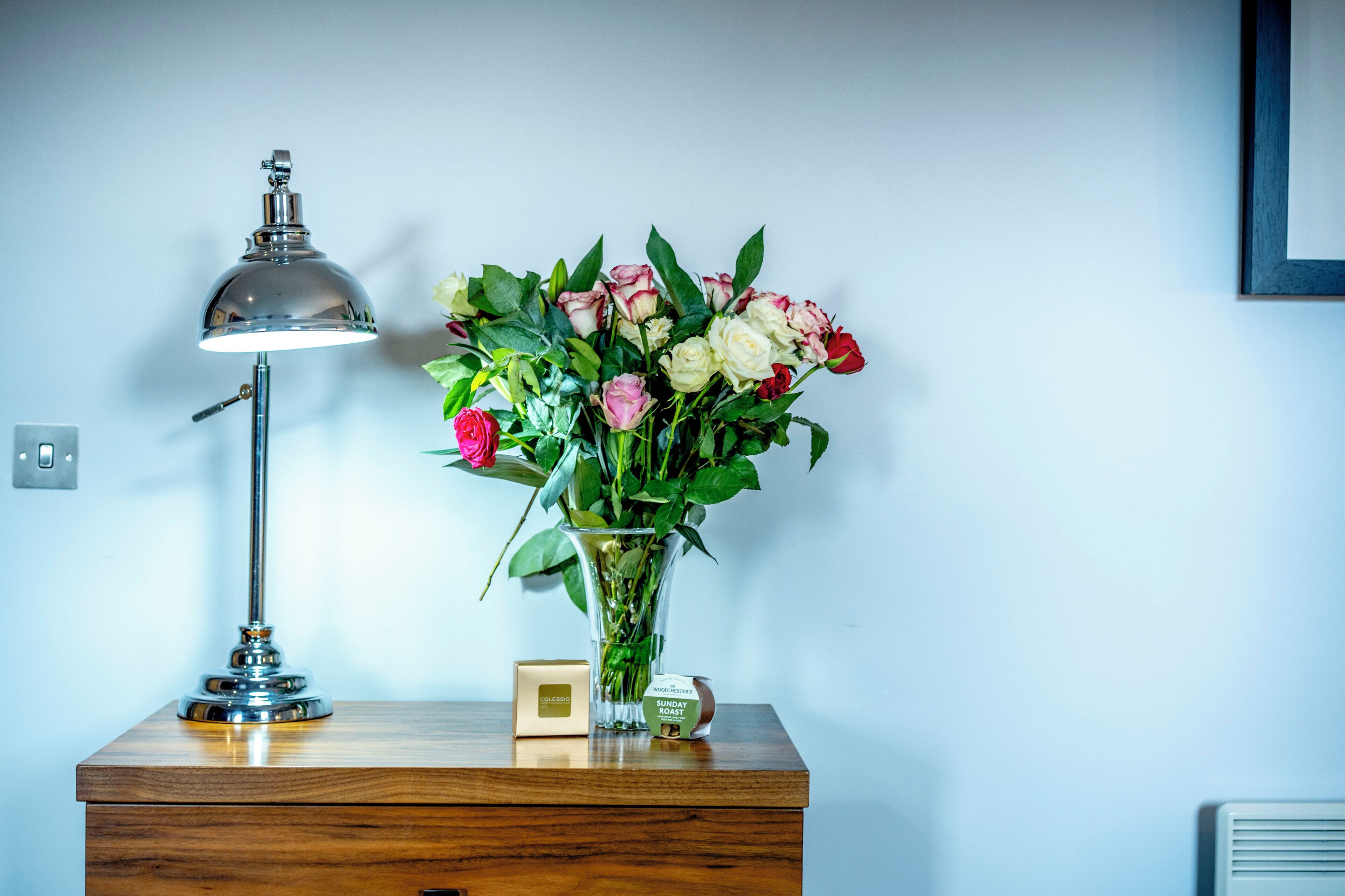 A desk with a lamp, a vase of flowers, and a small box.