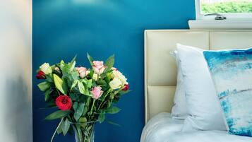 A bedroom with a bed, a bedside table with a vase of flowers, and a hanging light fixture.