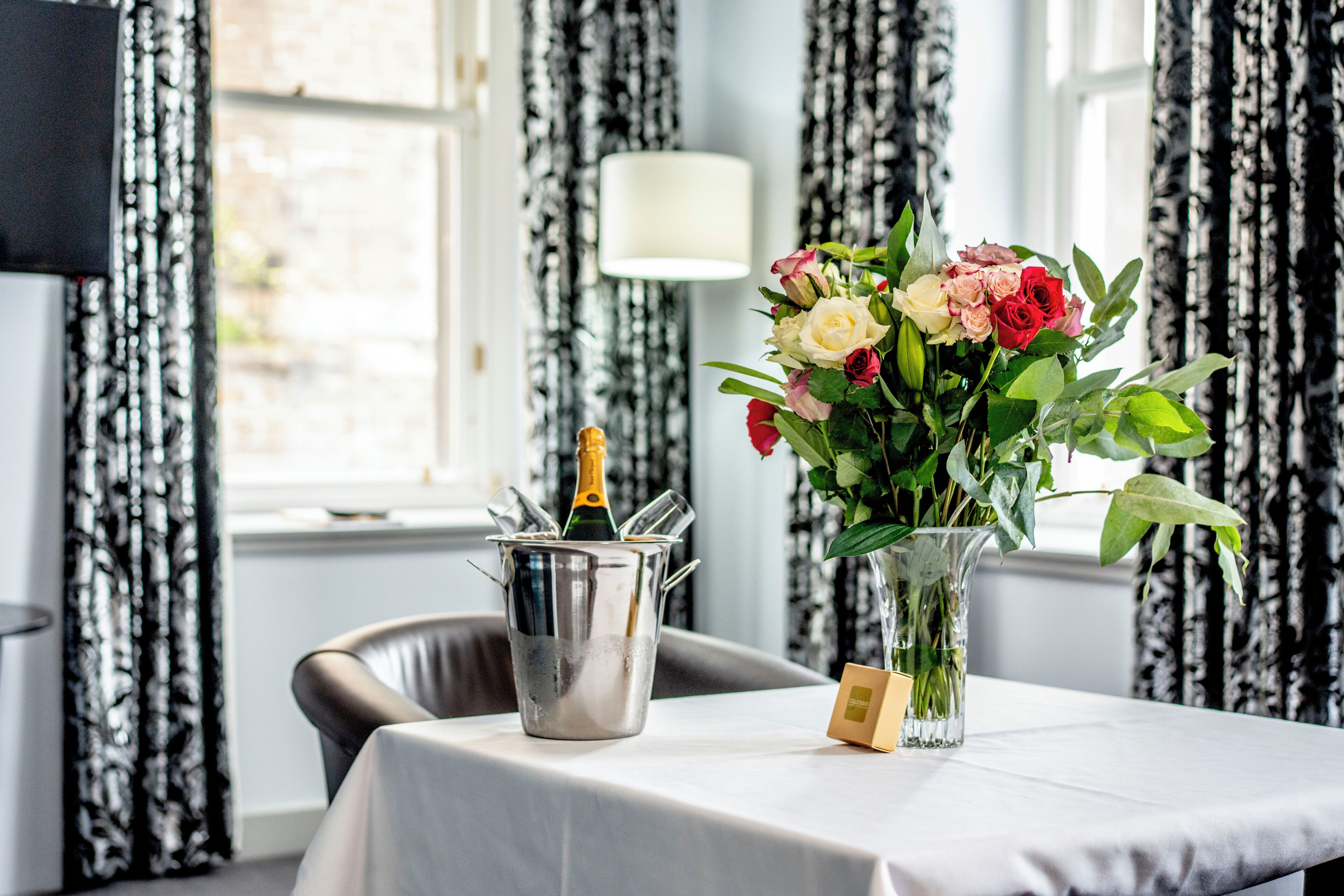 Een tafel met een champagnefles in een metalen emmer en een vaas met bloemen.