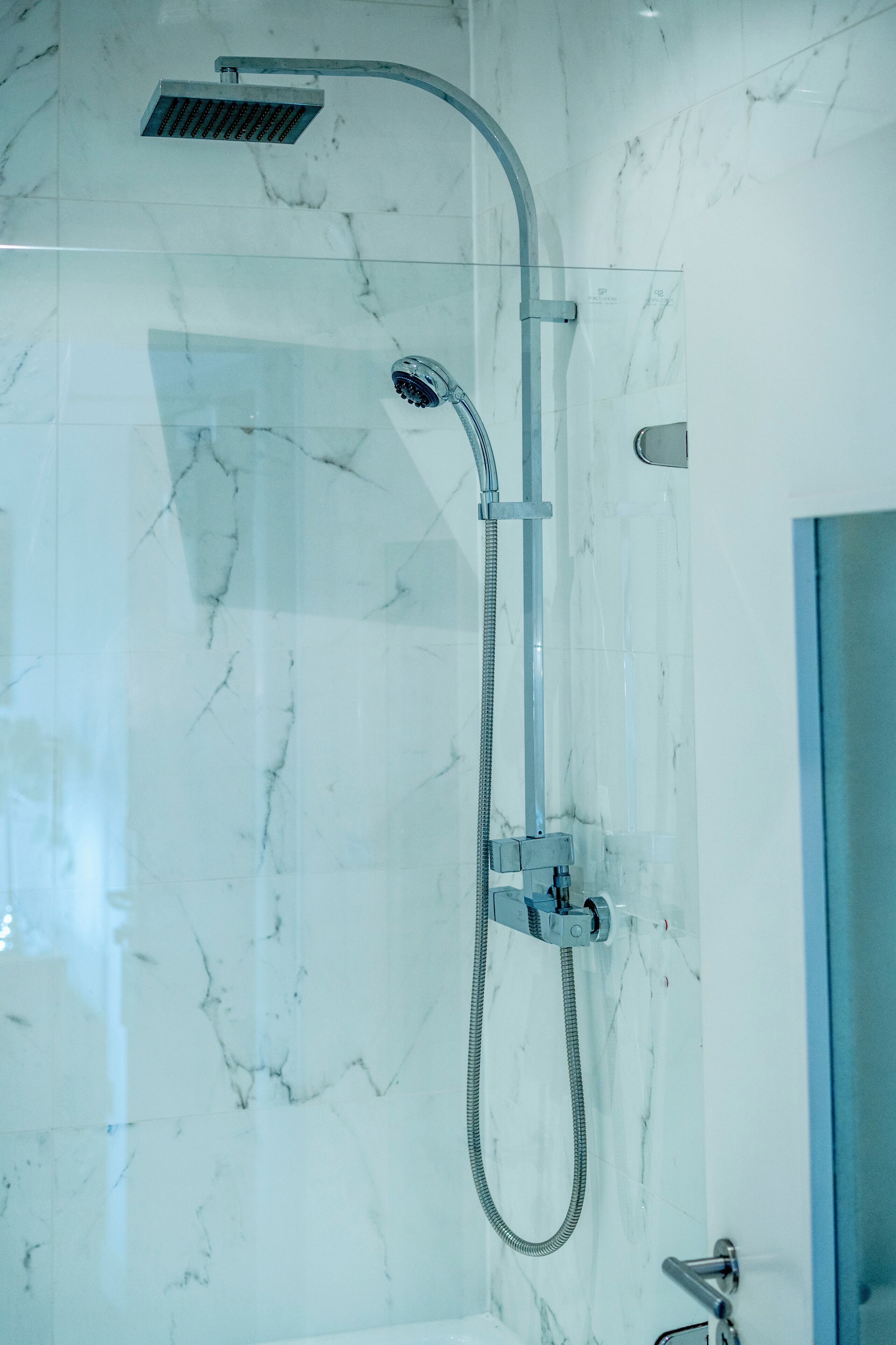 Un baño moderno con cabina de ducha de vidrio, paredes de mármol y puerta a la vista.