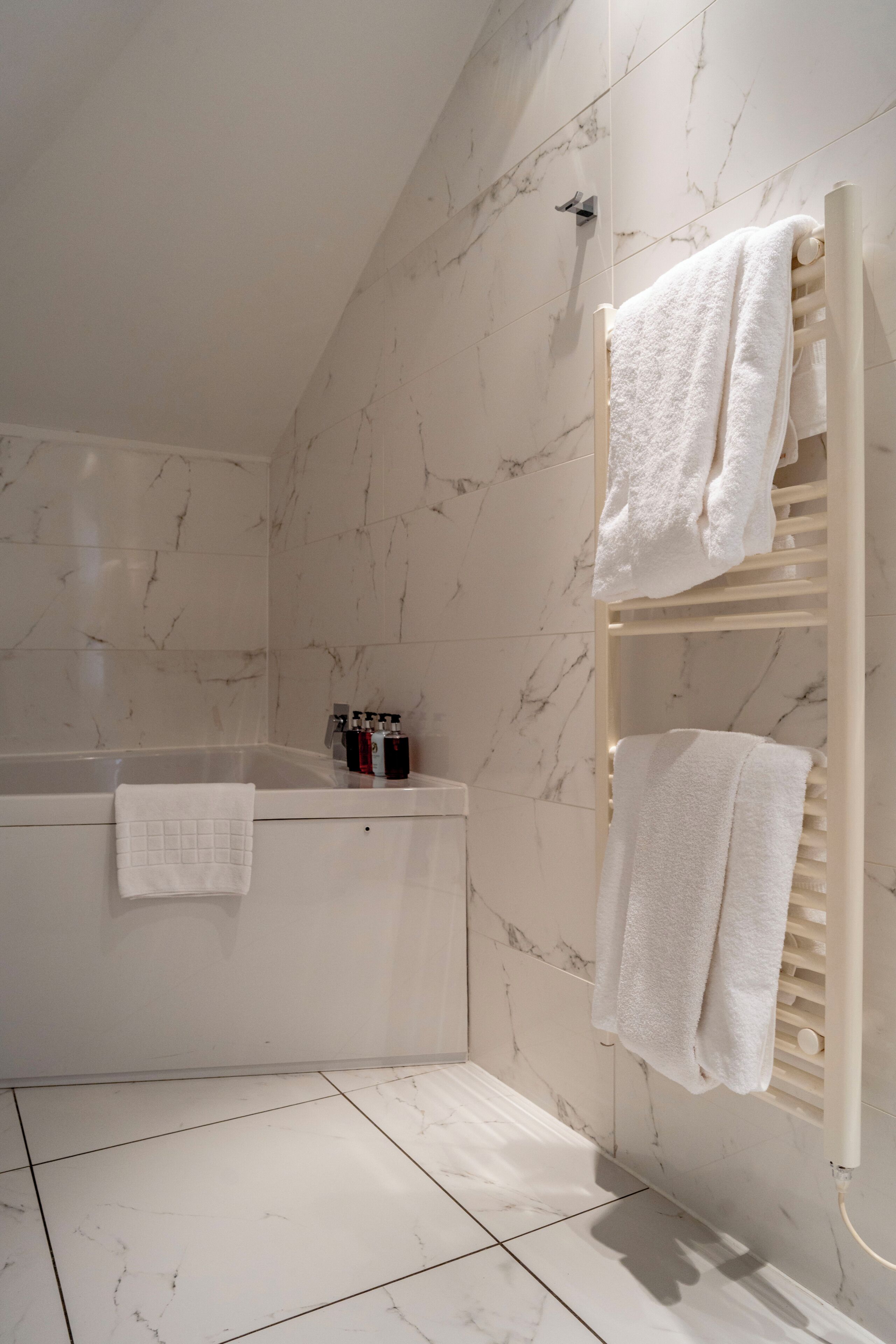 A bathroom with a bathtub, marble walls, and a towel rack.