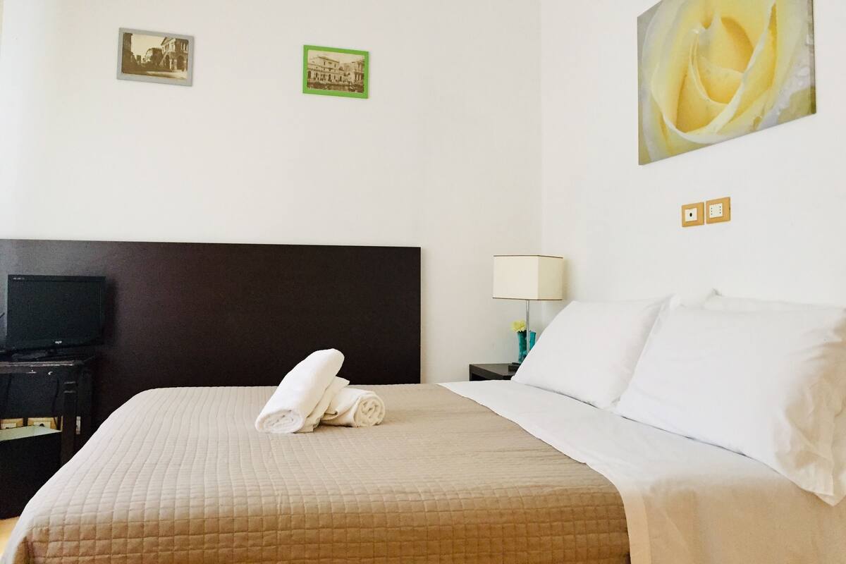 A hotel room with a bed, a TV, a lamp, and two pictures on the wall.