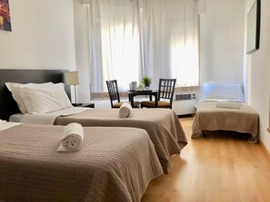 A hotel room with two beds, a desk, a chair, and a table with a plant. - L'Affittacamere di Venezia (Mestre)