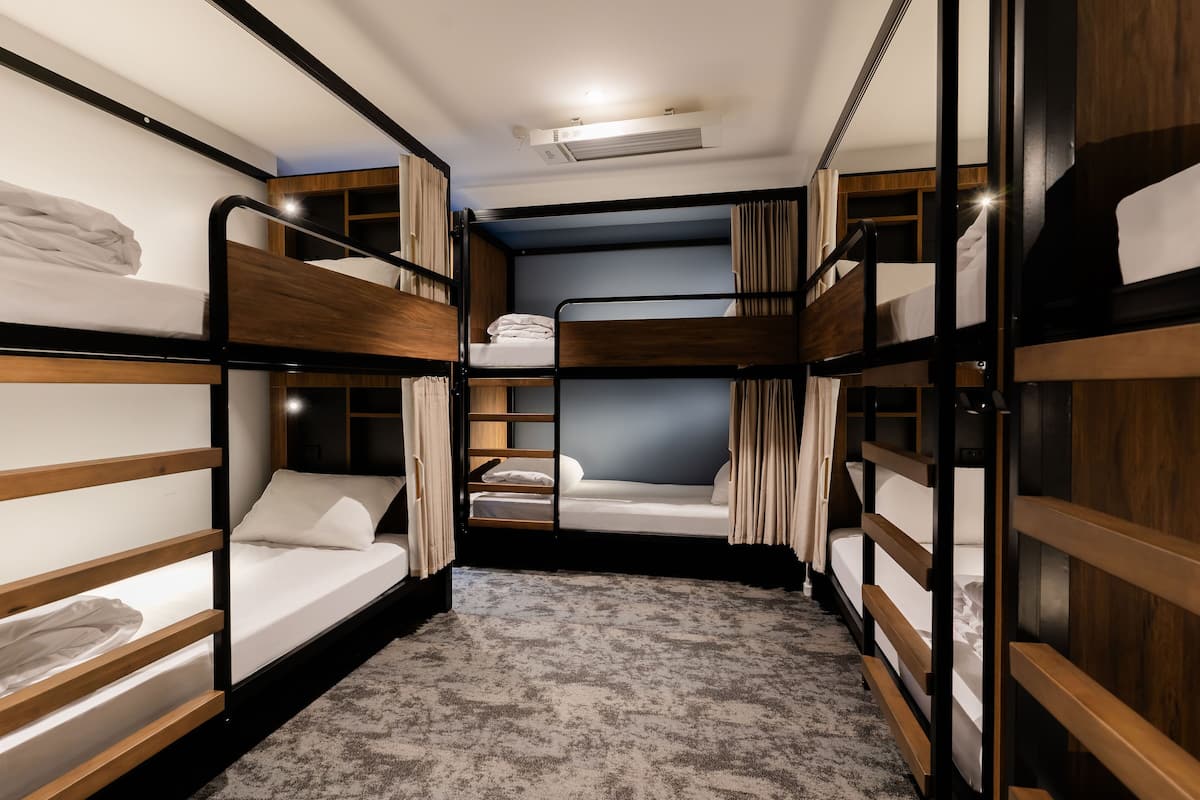 Een slaapzaal met drie stapelbedden, een plafondventilator en een vloerbedekking.