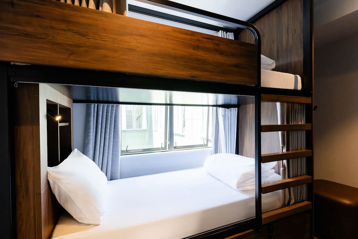 Een stapelbed met een houten hoofdeinde, een raam met gordijnen en een nachtkastje.