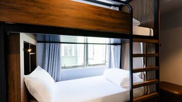 A bunk bed with a wooden headboard, a window with curtains, and a bedside table.