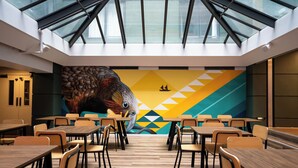 A modern restaurant with a high ceiling, geometric wall art, and a skylight. Tables and chairs are arranged for dining. - Haka House Wellington (Wellington)