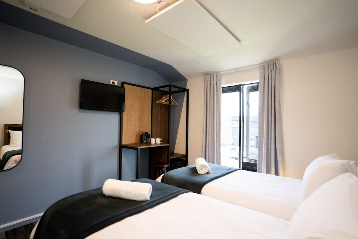 Een hotelkamer met twee bedden, een televisie, een bureau en een raam met gordijnen.
