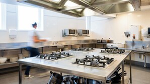 A modern kitchen with stainless steel appliances, a large island with gas stoves, and a window providing natural light. - Haka House Wellington (Wellington)