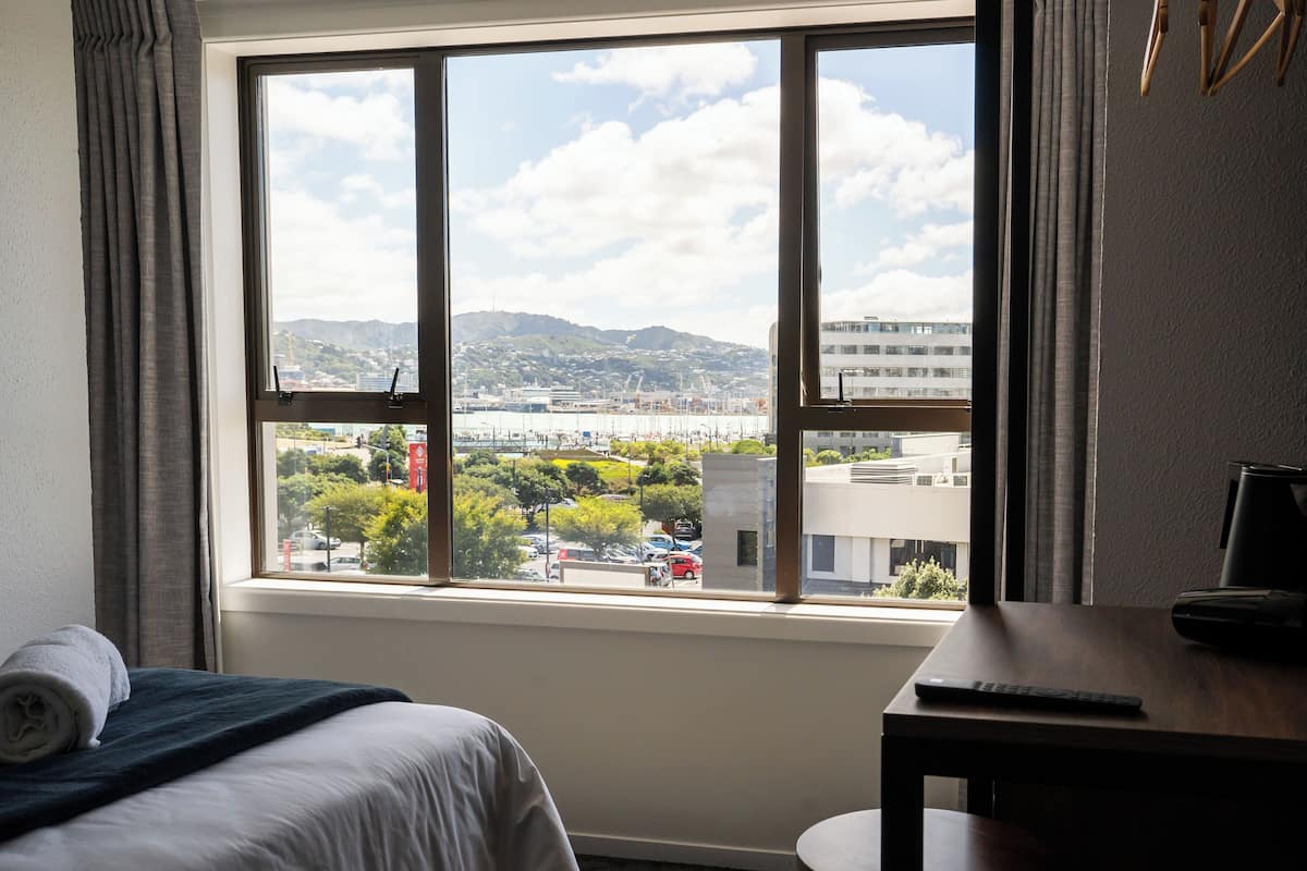 Een hotelkamer met een groot raam dat uitzicht biedt op een stadsbeeld, een bed met een netjes gevouwen handdoek en een bureau met een afstandsbediening.