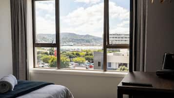 A hotel room with a large window offering a view of a cityscape, a bed with a neatly folded towel, and a desk with a remote control.