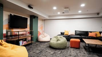 A modern living room with a flat-screen TV, a sofa, bean bags, and a bookshelf.