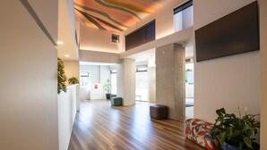 A spacious hallway with wooden flooring, a modern ceiling design, and a seating area with a colorful sofa and potted plants. - Haka House Wellington (Wellington)