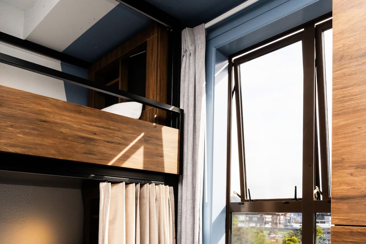 Een stapelbed met een raam, een klein voetenbankje en een plafond met een geometrisch patroon.