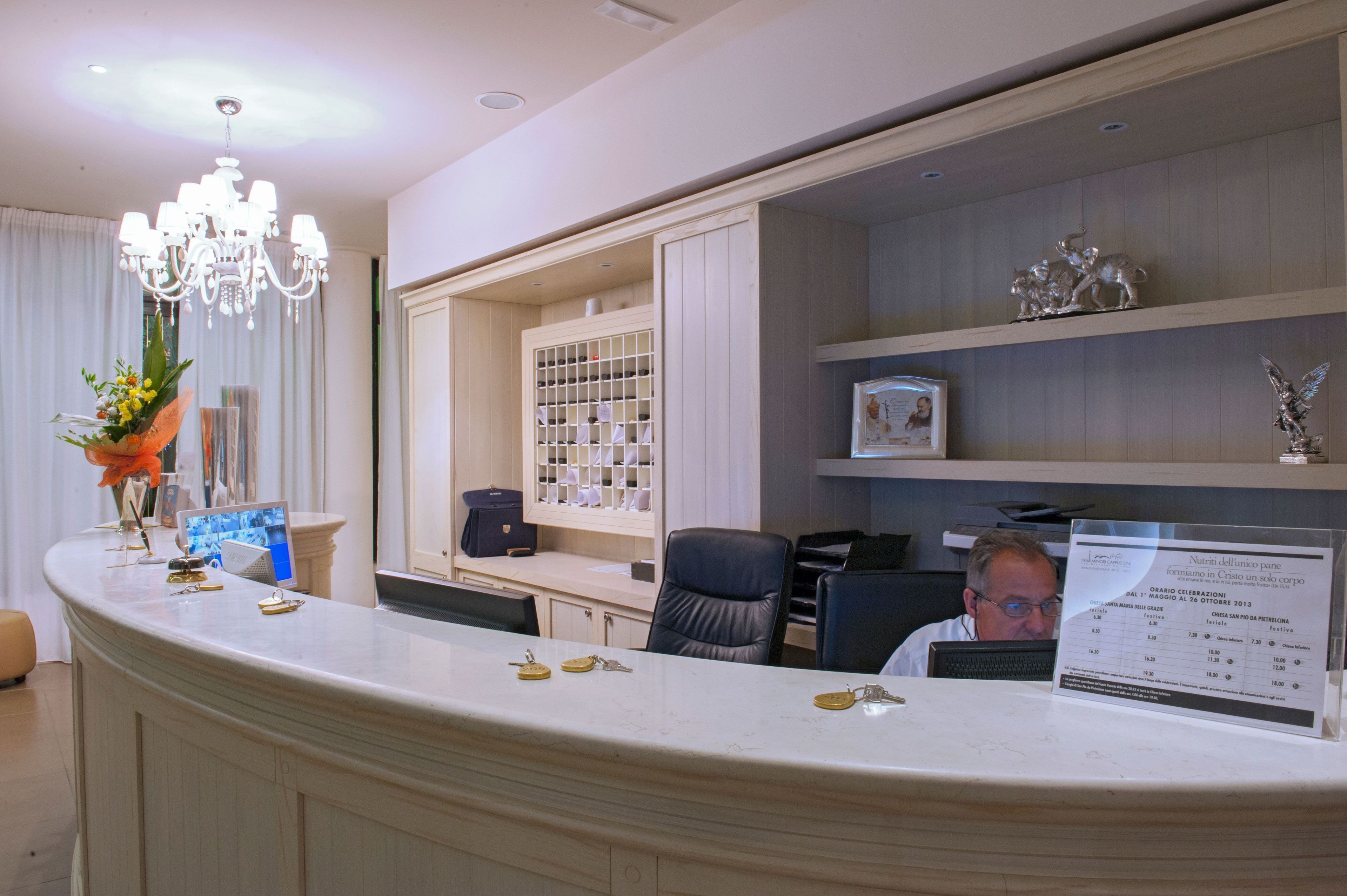 A reception desk with a chandelier, a counter with keys, a framed photo, and a bulletin board with a menu.