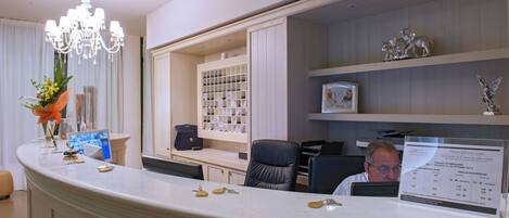 A reception desk with a chandelier, a counter with keys, a framed photo, and a bulletin board with a menu.