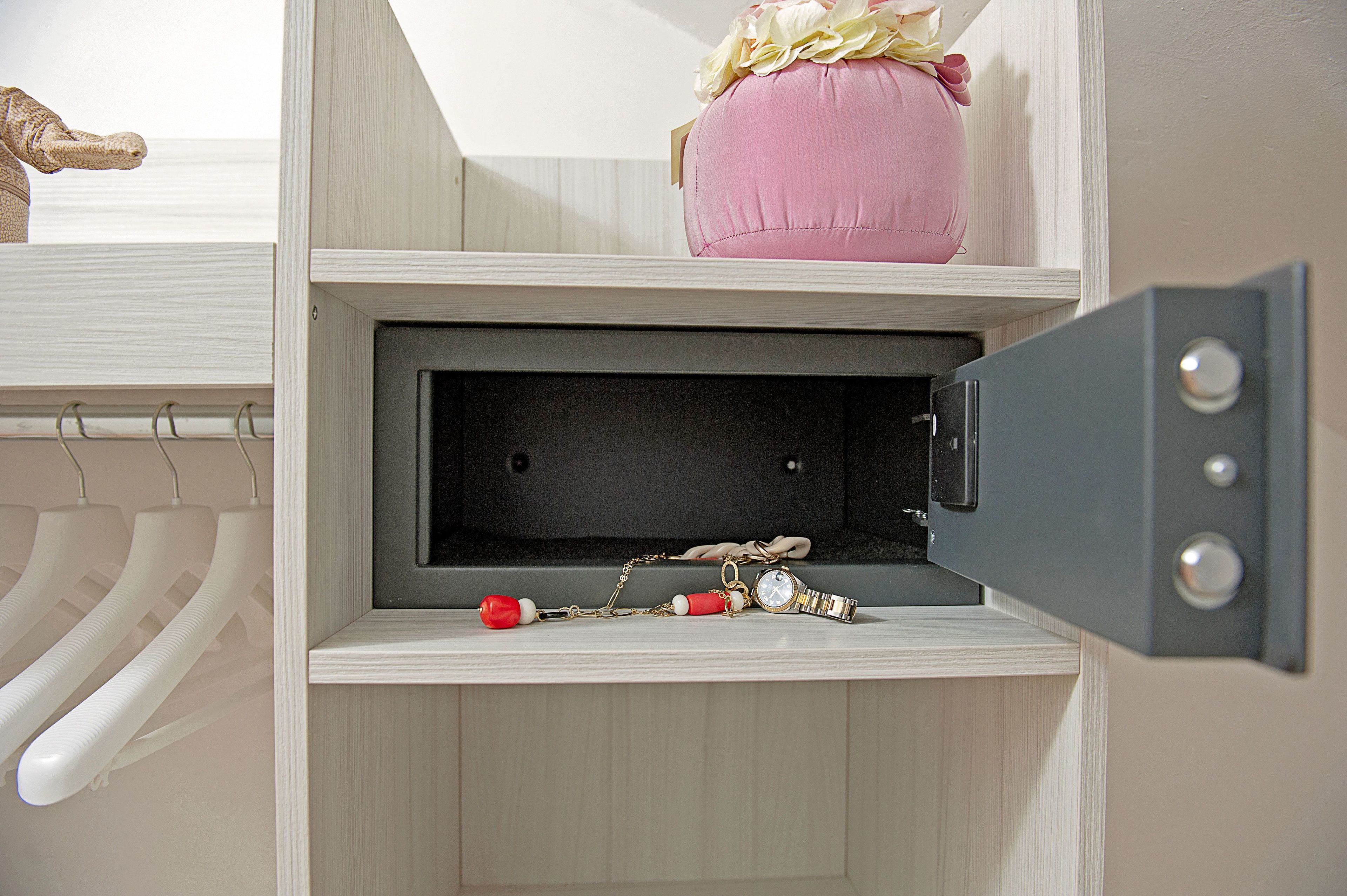 A storage unit with a pink cushion, a watch, and a red object.