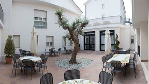 A courtyard with outdoor seating, a tree, and a building with balconies. - Hotel Fini (San Giovanni Rotondo)