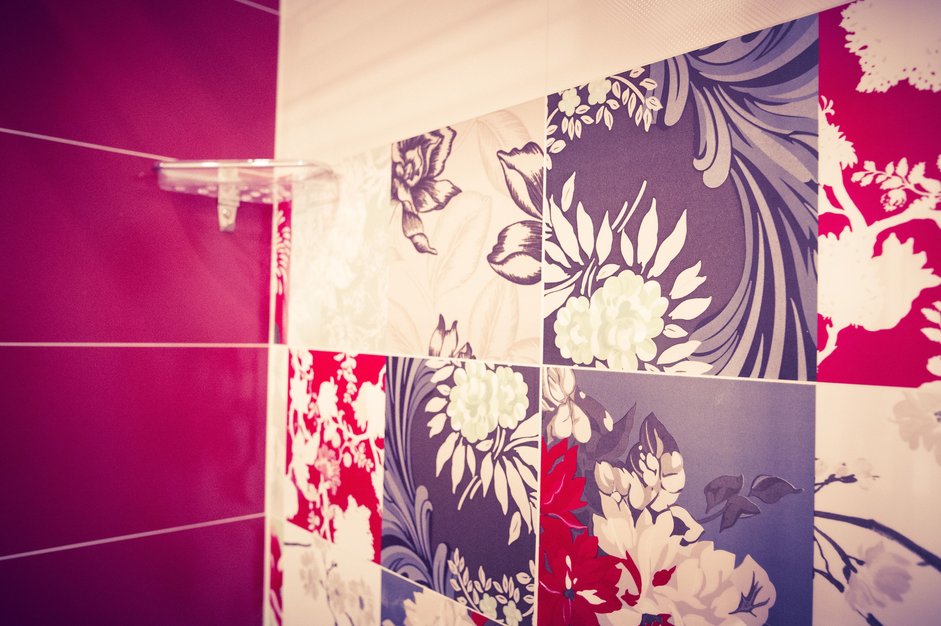 Casa de banho com azulejos florais vermelhos e azuis na parede.