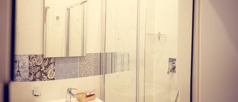 A modern bathroom with a glass shower enclosure, a sink with a mirror above it, and a small stool.