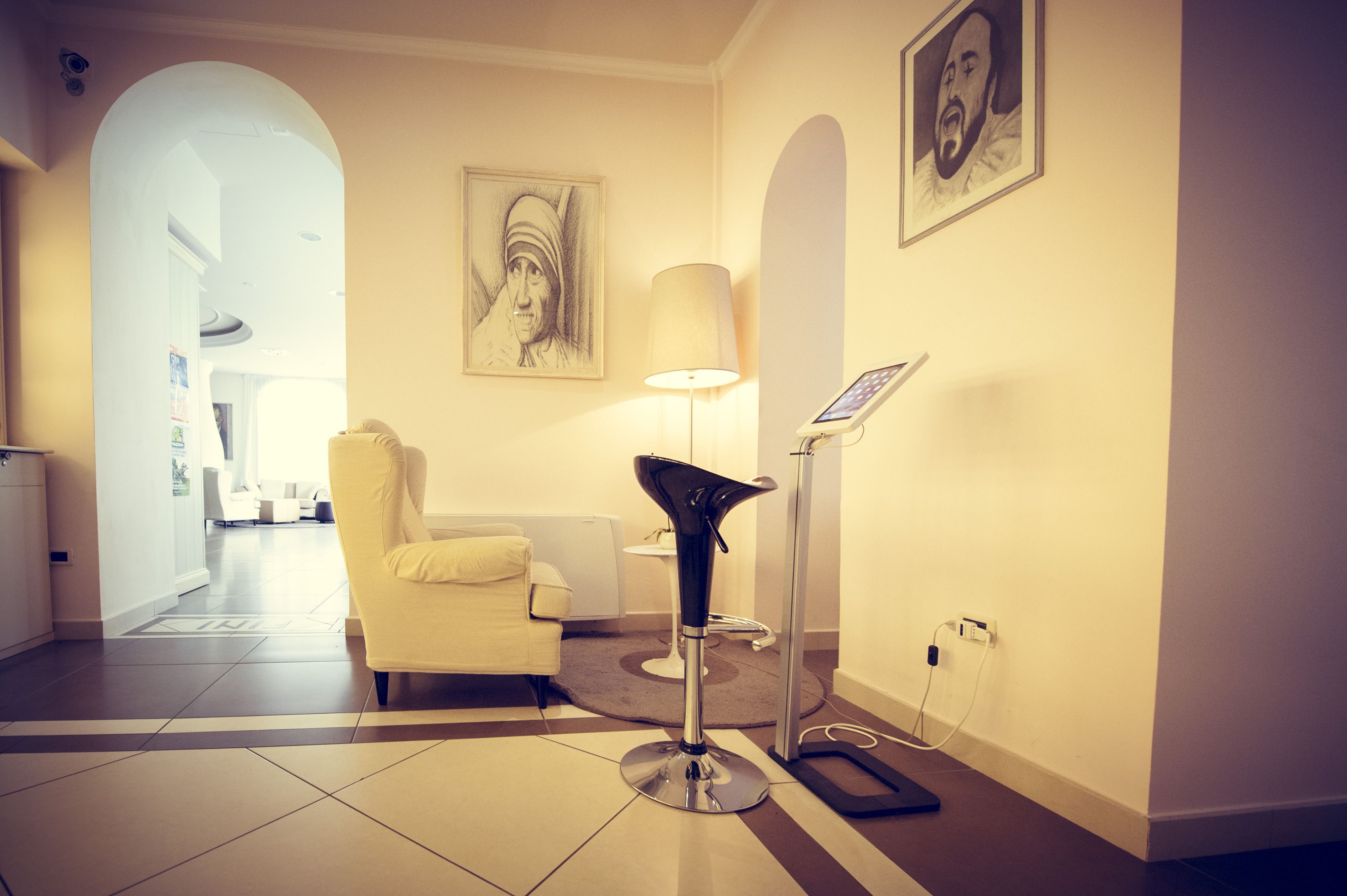 Hall d'hotel con una poltrona moderna, una lampada da terra e un ritratto incorniciato appeso al muro.