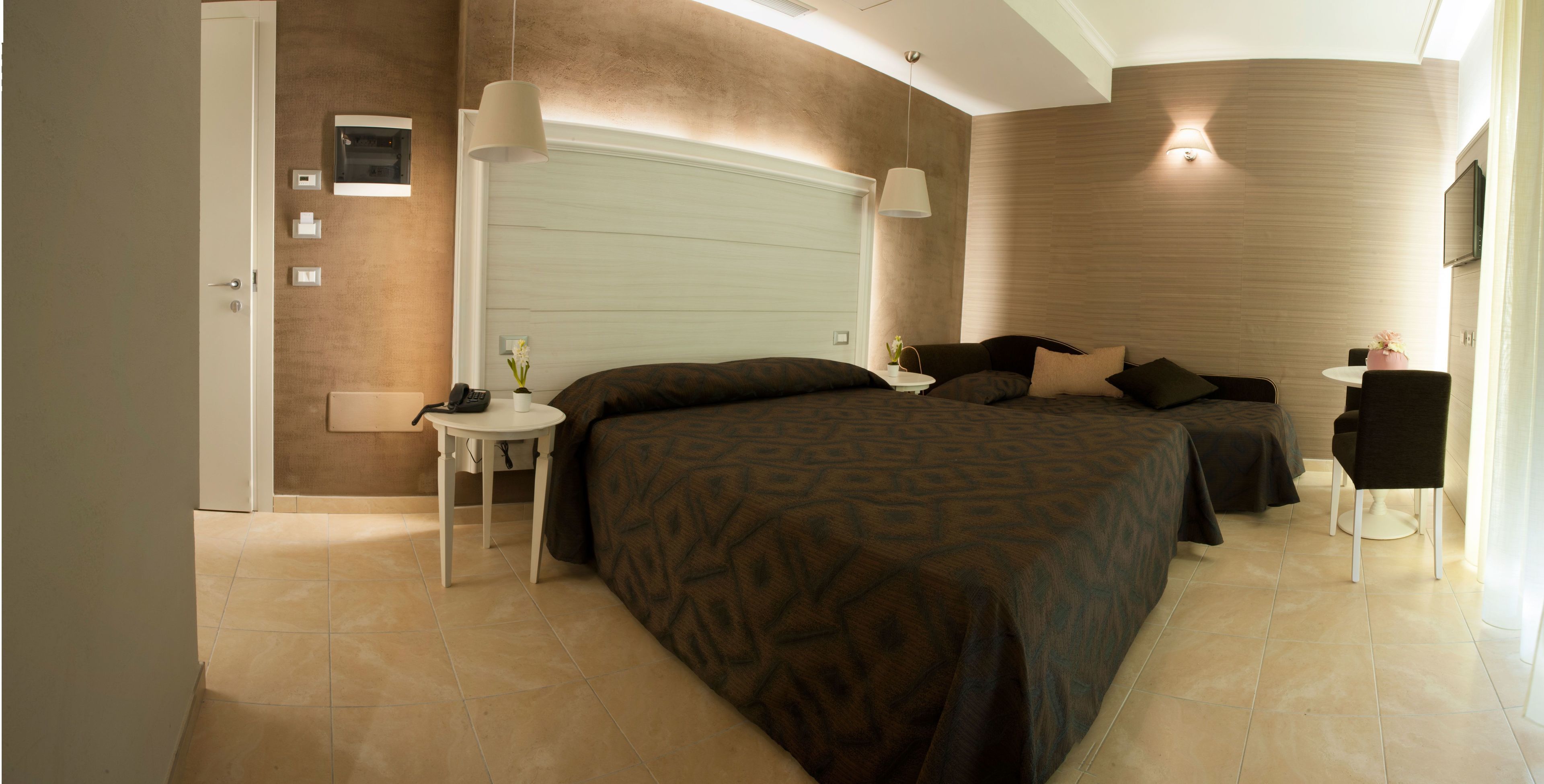 A modern bedroom with a large bed, bedside tables, a small table with a vase, and a chair.