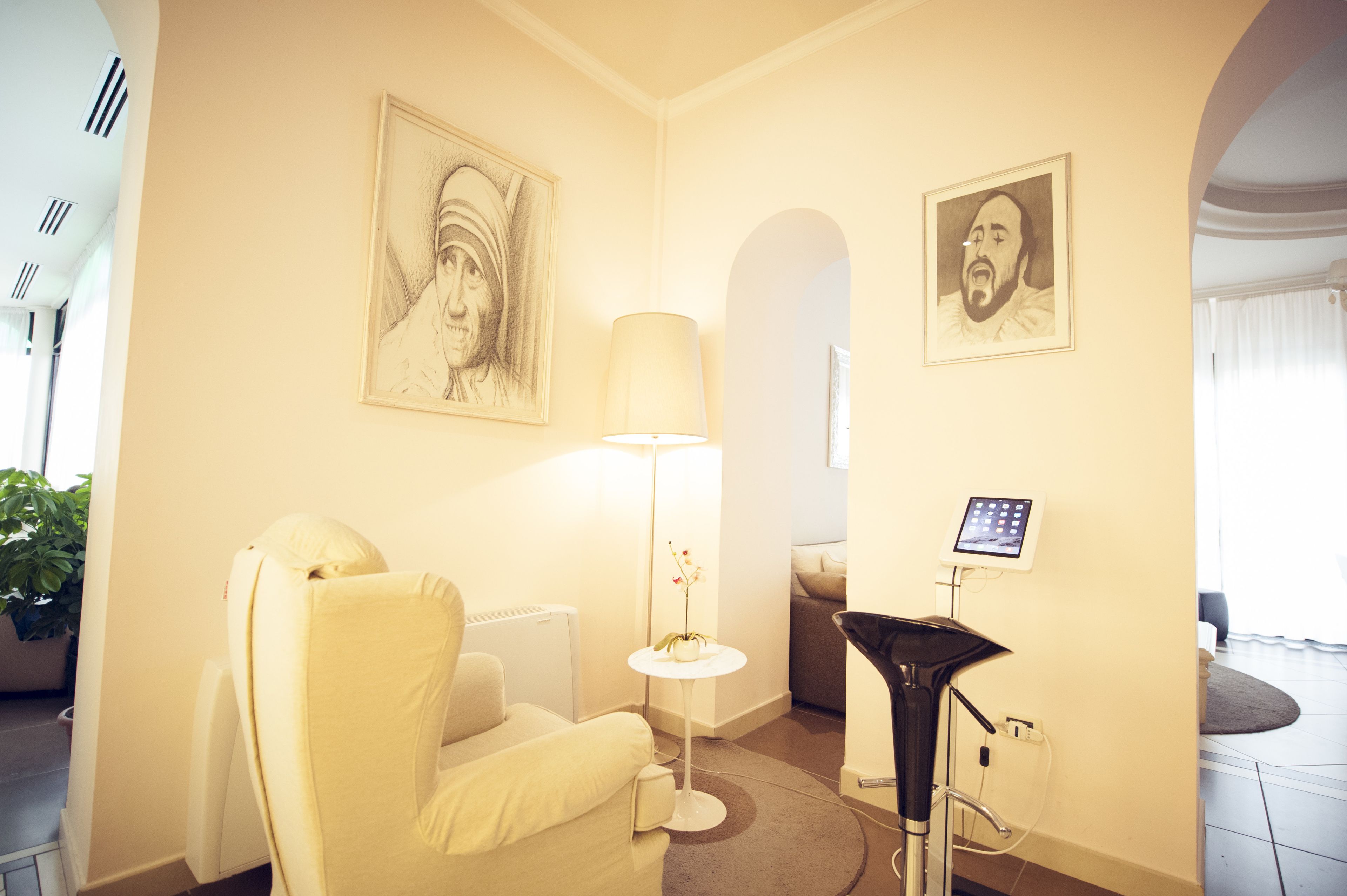 A room with a massage chair, a standing massage table, a lamp, and two framed portraits on the wall.