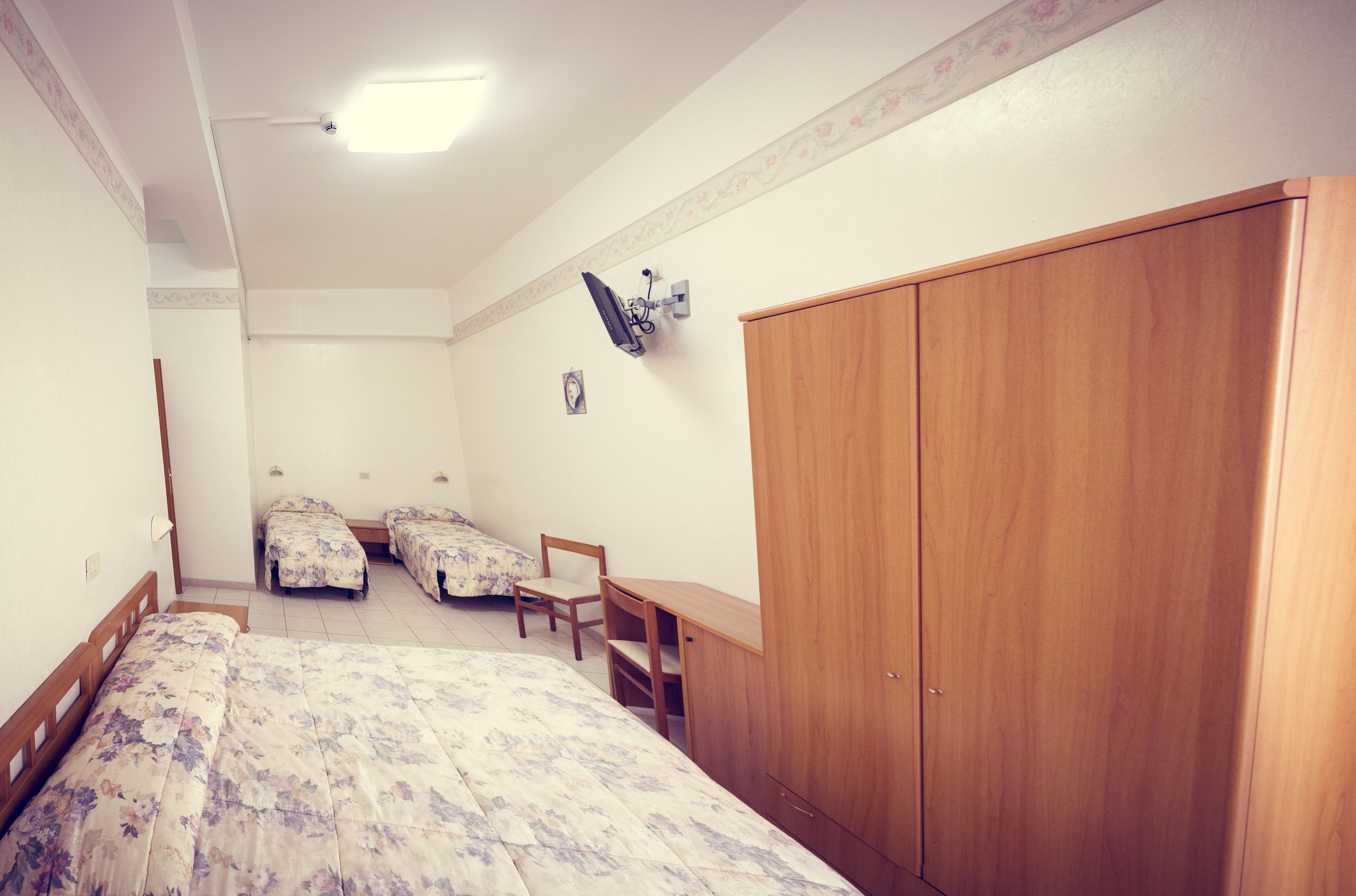 A bedroom with a large bed, two single beds, a wooden wardrobe, a desk, and a chair.