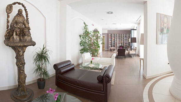 A spacious lobby with a brown leather sofa, a glass coffee table, and a white pillar. - Hotel Fini (San Giovanni Rotondo)