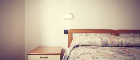 A bedroom with a wooden bed, a nightstand with a drawer, and a wall-mounted light fixture.