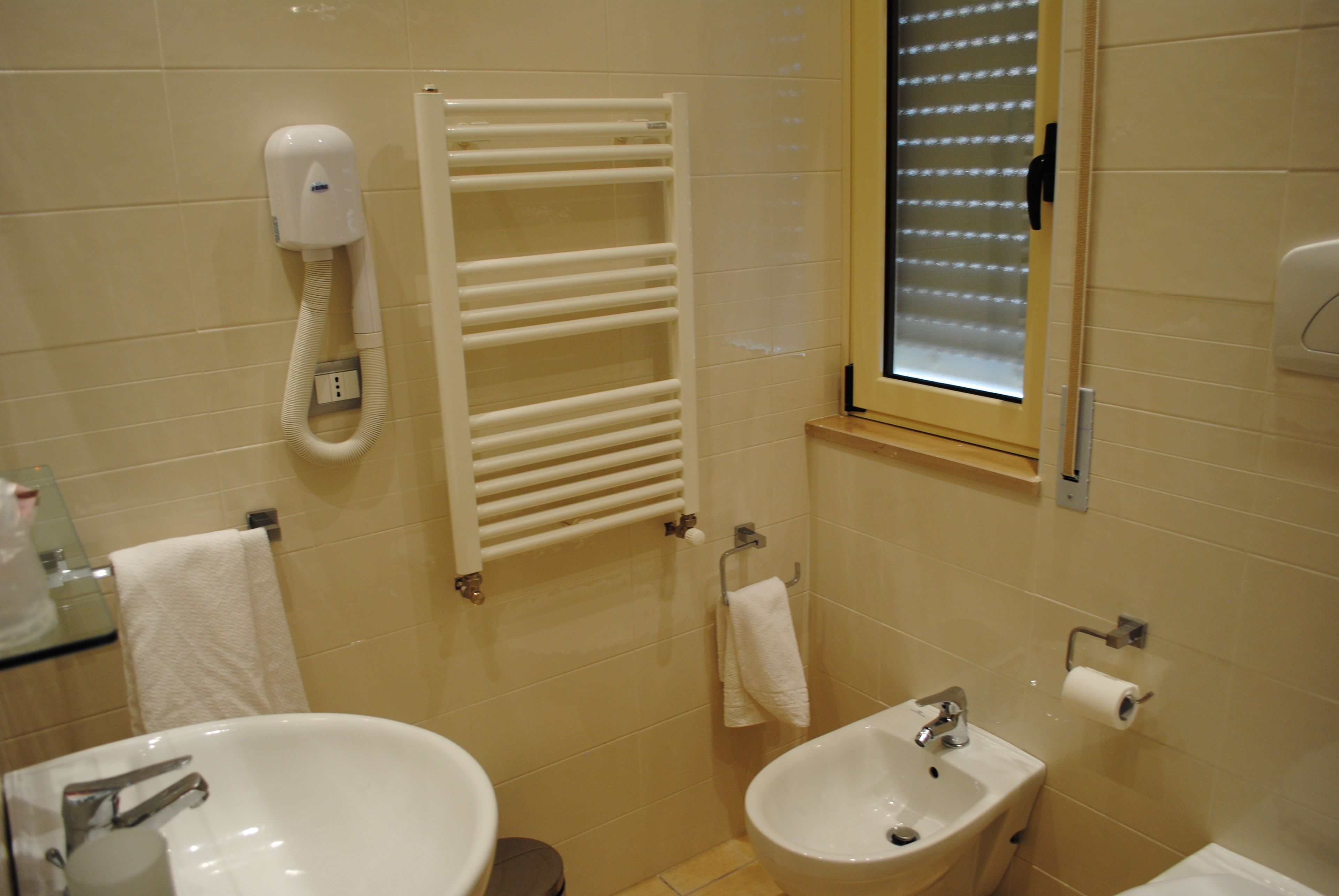 A bathroom with a sink, bidet, towel rack, and a hand dryer.