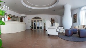 A spacious lobby with a reception desk, seating area, and large windows. - Hotel Fini (San Giovanni Rotondo)