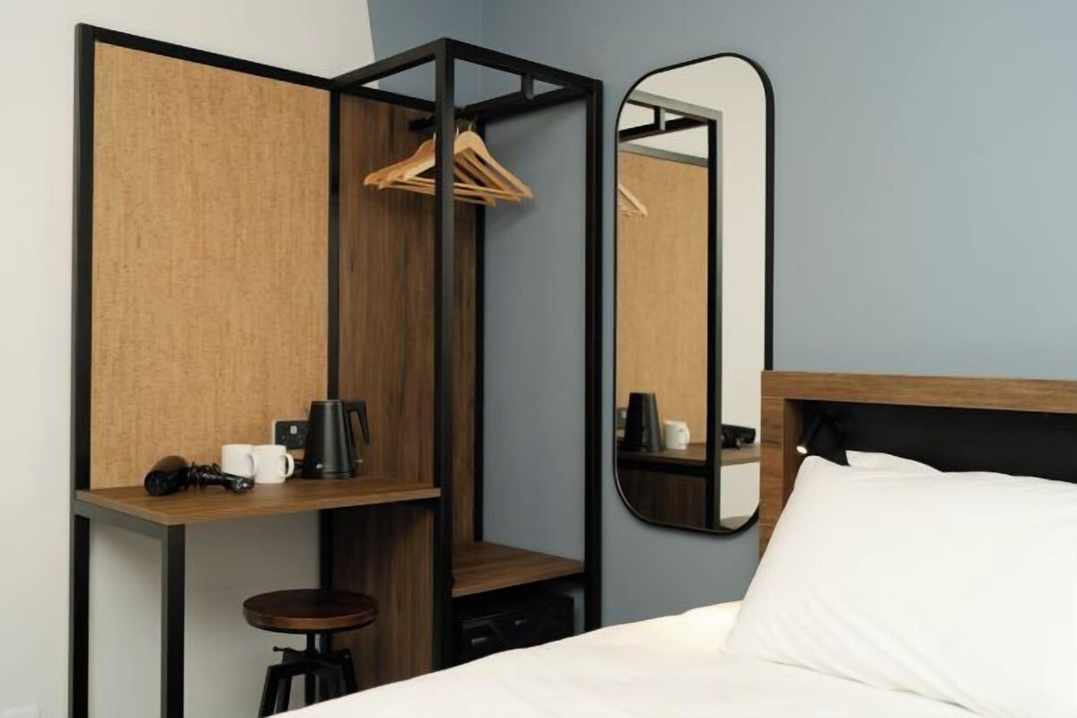 Una habitación de hotel con una cama, un escritorio de madera, un espejo y un perchero.