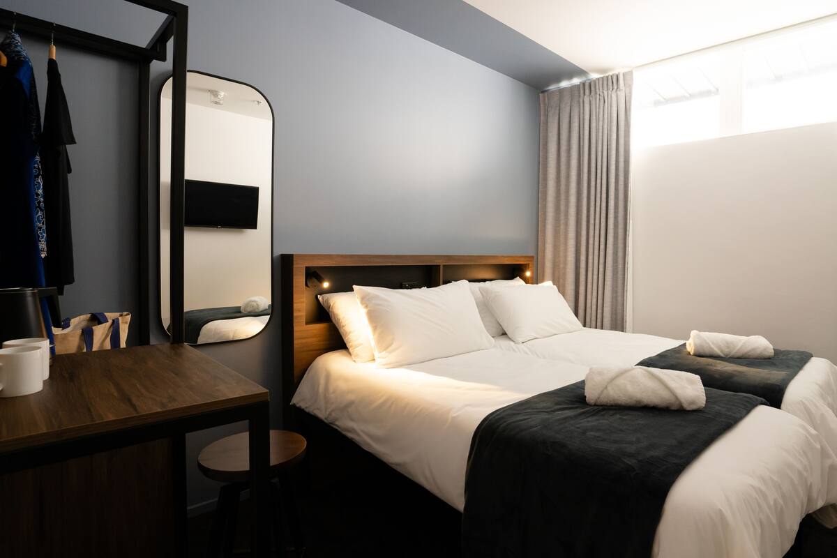 A hotel room with a bed, a desk, a mirror, and a window with curtains.