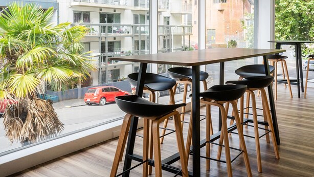 A modern interior with a wooden table and black chairs, large windows offering a view of a cityscape and a red car outside. - Haka House Auckland City (Auckland)