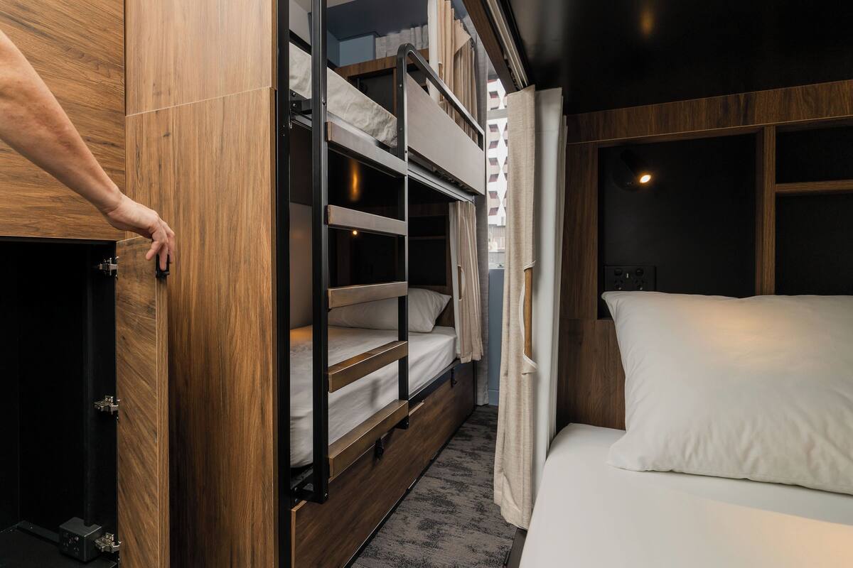 A bunk bed with a wooden frame and a white mattress, a single bed with a white mattress, and a wooden door with a handle.