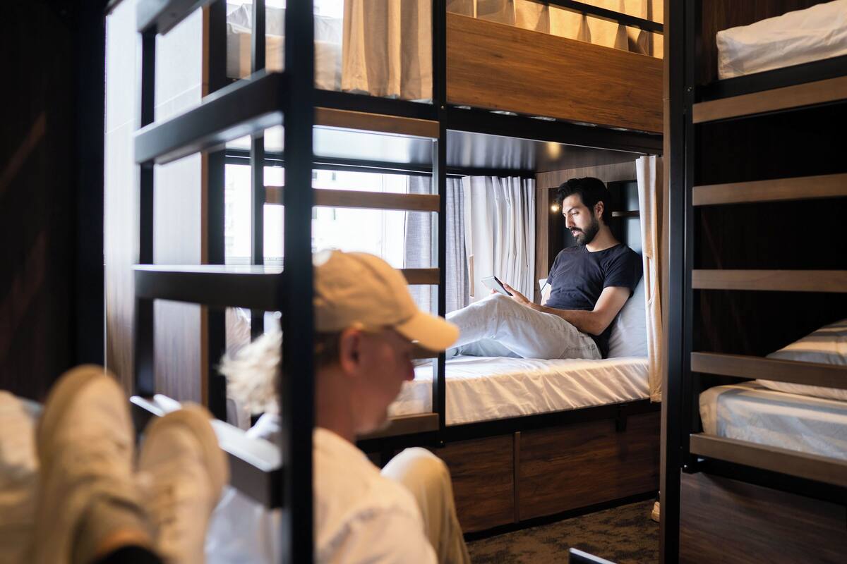 A bunk bed room with a window, a bedside table, and a chair.