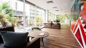 A modern hotel lobby with a wooden floor, leather seating, and large windows offering a view of the city. - Haka House Auckland City (Auckland)