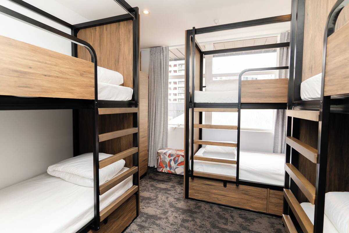 A bunk room with wooden bunk beds, a small table, and a window with curtains.