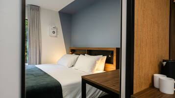 A modern hotel room with a neatly made bed, a wooden nightstand, and a small table with two white mugs.