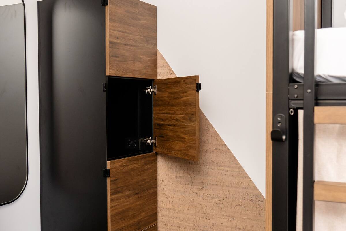 A compact room with a built-in wardrobe, a small leather ottoman, and a partial view of a bed.