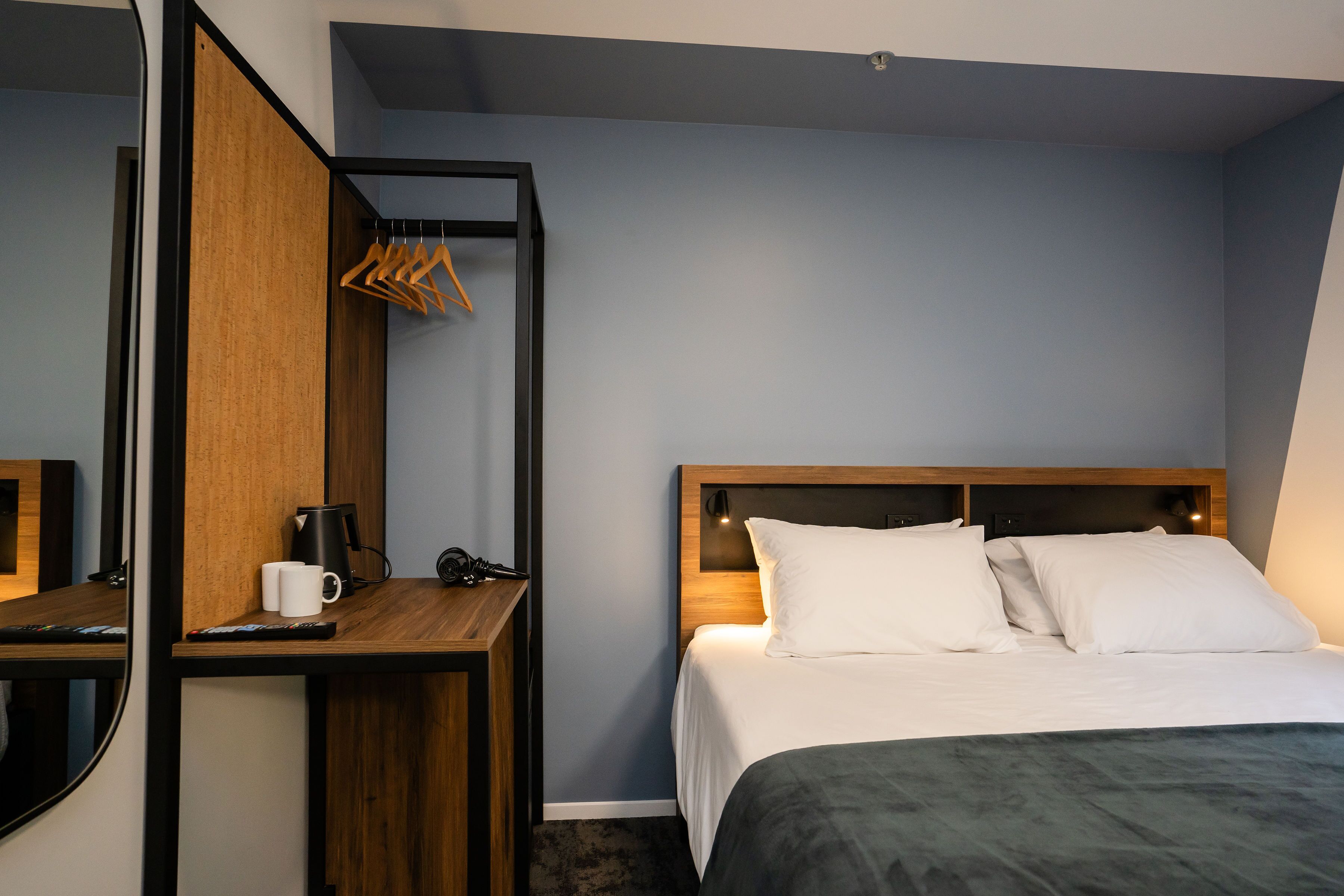 Een hotelkamer met een bed, een bureau met koffiezetapparaat, een spiegel en een kapstok.
